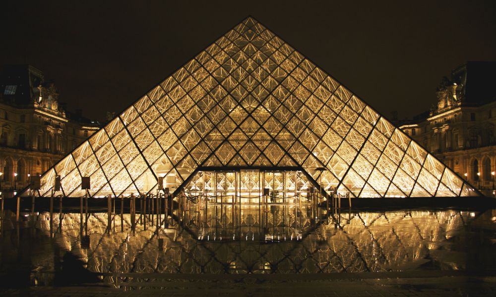 This is an image of the Louvre at night time with all its lights on and no people lining up outside.