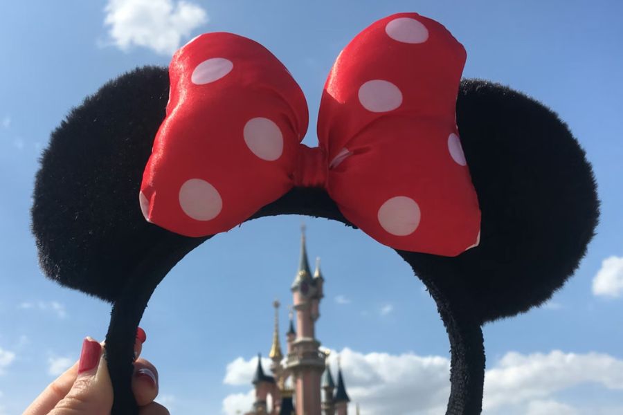 This is an image of a lady holding up Mickey Mouse ears with the castle behind it.