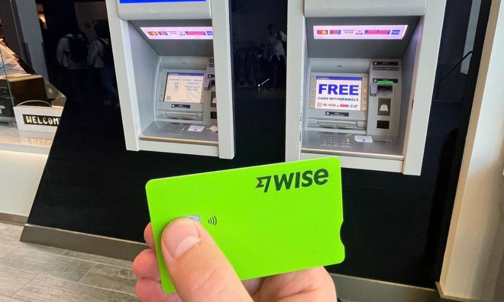 How to avoid fees when using your card in Paris: This is an image of someone holding up their green Wise card in front of two overseas ATMs.