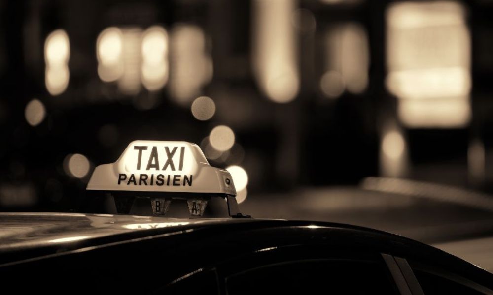 This is an image of the top of a taxi in Paris that says Taxi Parisien. It is dark and the taxi light is on.