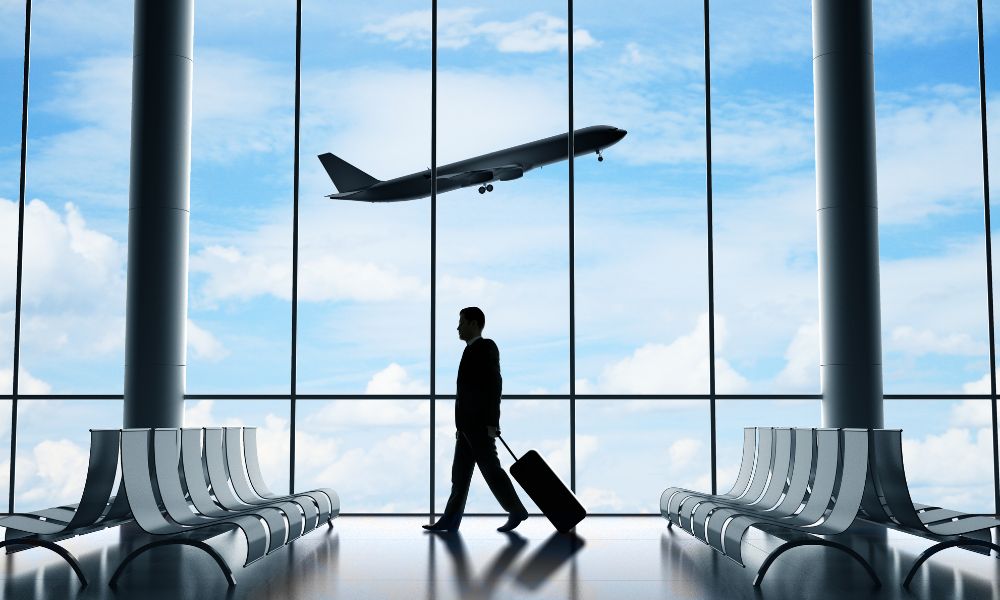 This is an image of a man walking on the tarmac, the plane is flying up above from the window behind him.