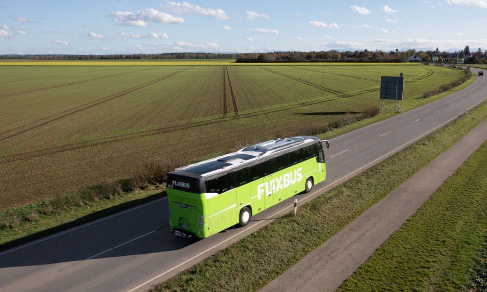 This is an image of a Flixbus travelling through a country road with flat greenery all around them.