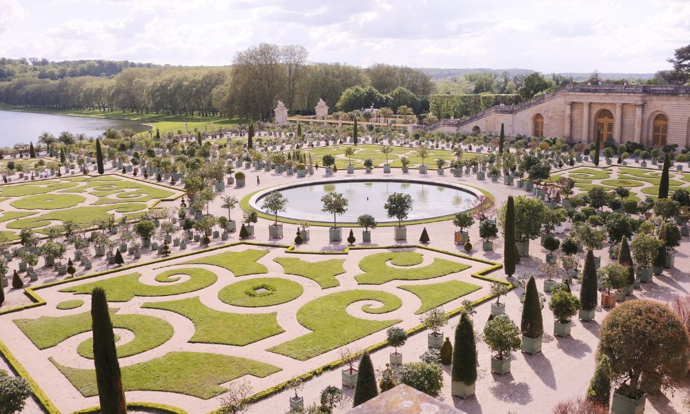 This is an image of the gardens at the Palace of Versailles. You can see the pristine gardens and body of water in the centre, as well as some of the castle building.
