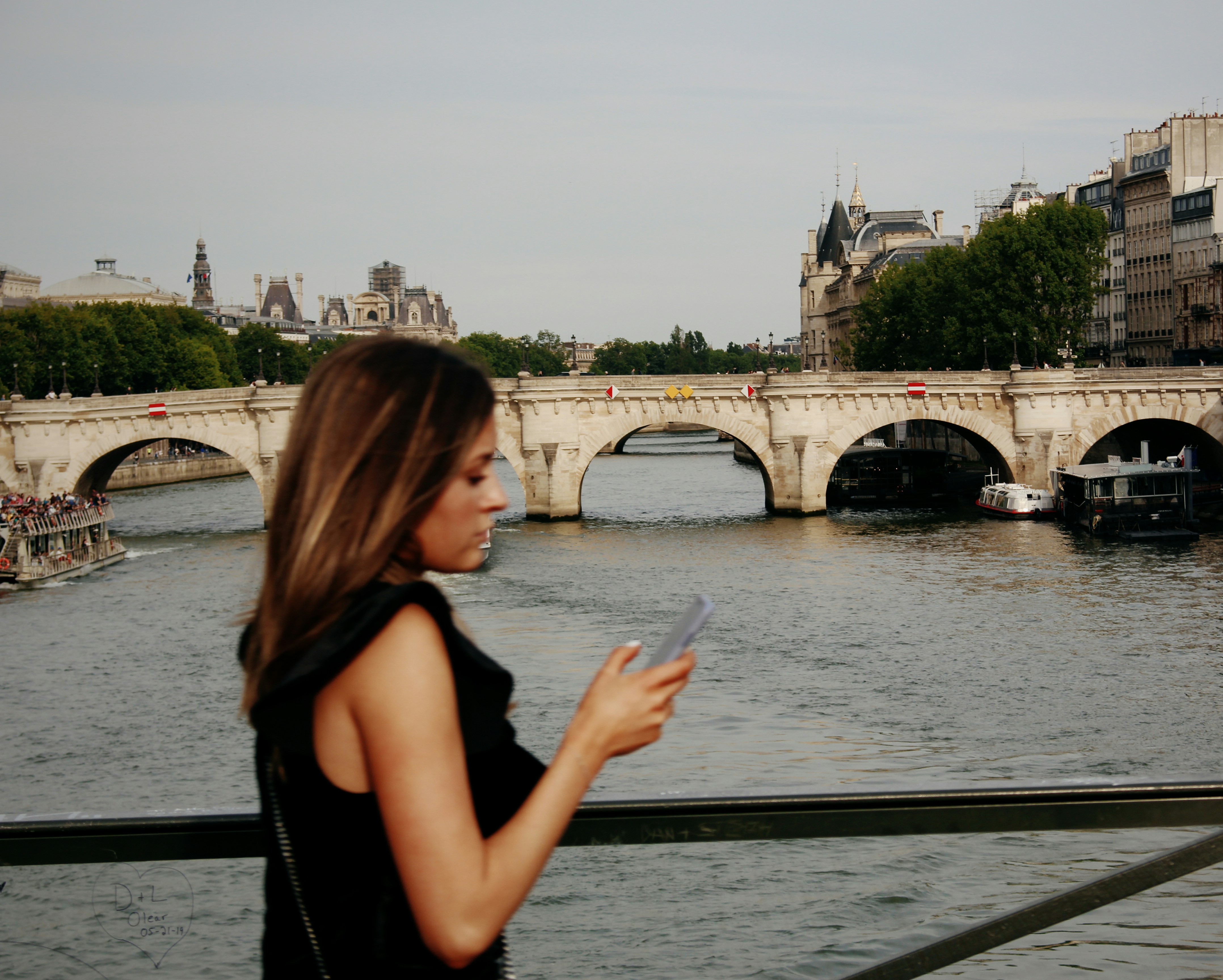 A woman walking across a bridge in Paris. She is looking at her phone.