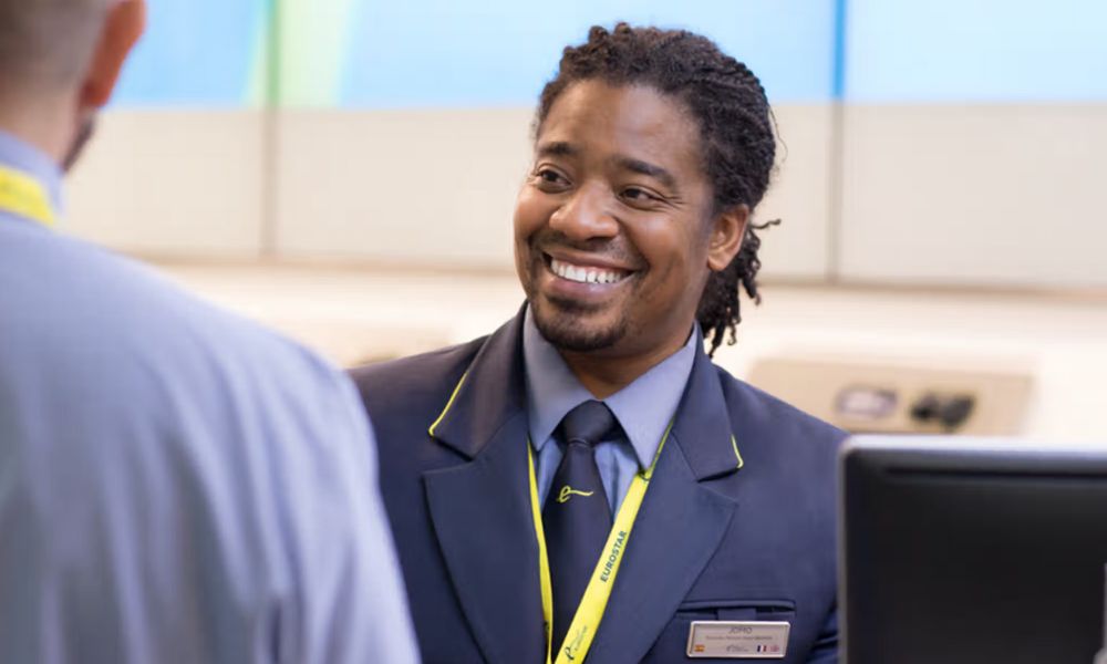 This is an image of a Eurostar worker talking and smiling at someone. He is wearing a suit and Eurostar lanyard.