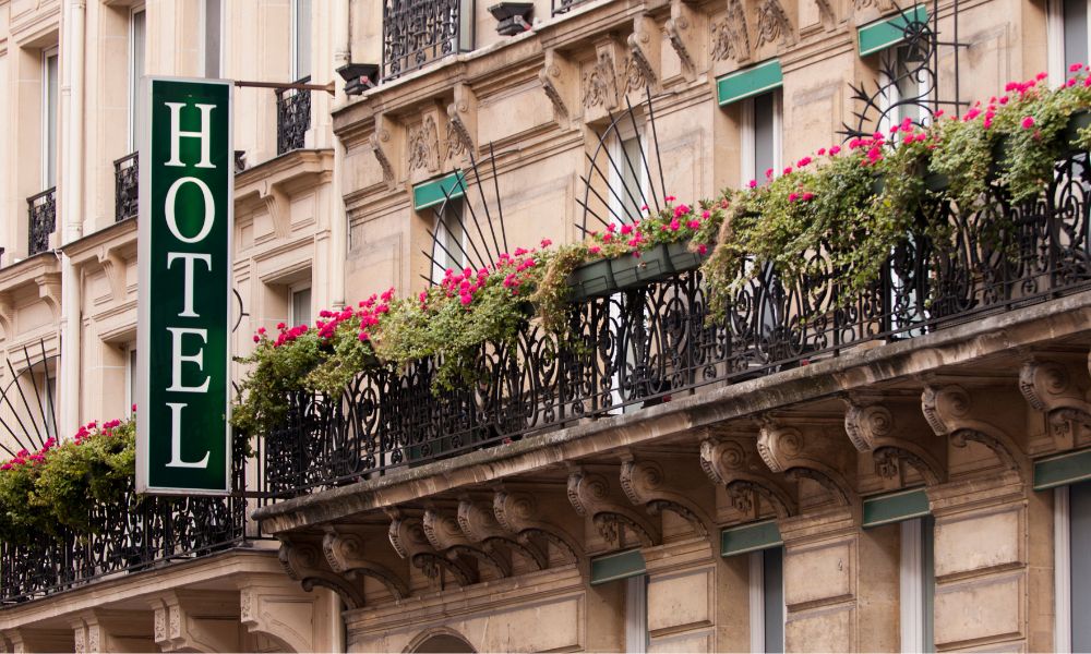 This is an image of the front of a hotel with a small balcony terrace and flower pots on them.