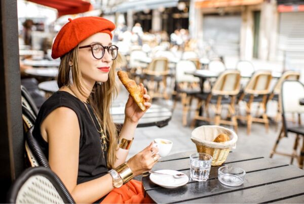 This is an image of a woman in a beret drinking a coffee and eating a croissant.