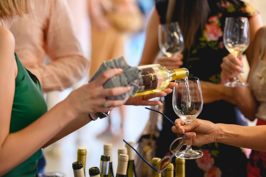 This is an image of a group of people holding wine glasses. One of the girls is holding the bottle pouring a drink for another person.