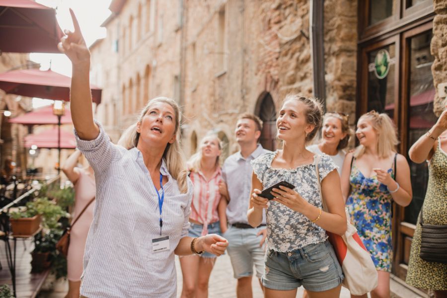 This is an image of a tour group looking up at buildings. The tour guide is pointing somewhere in the distance.