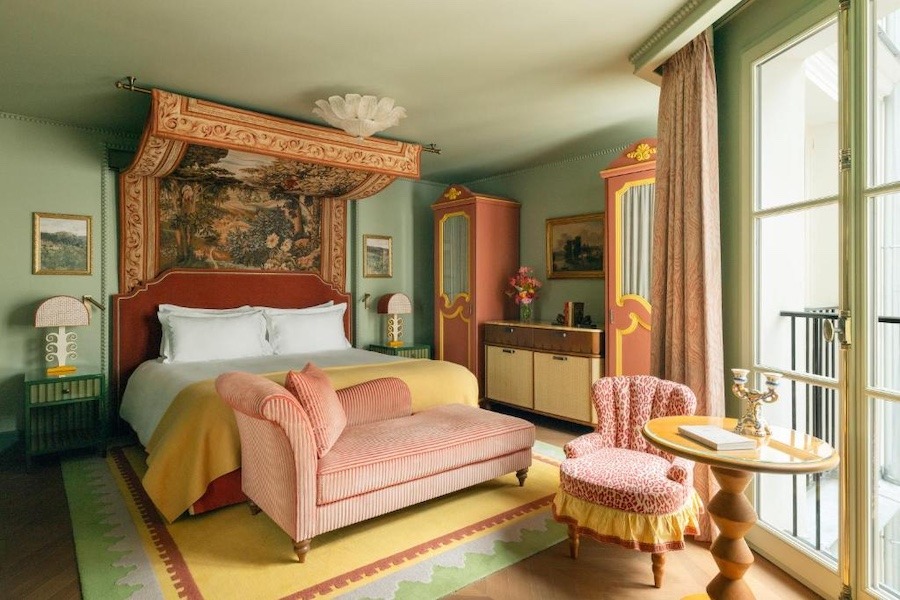 A colourful room with teal walls, a drapery above the bed, terracota coloured bed, and a pink chair.