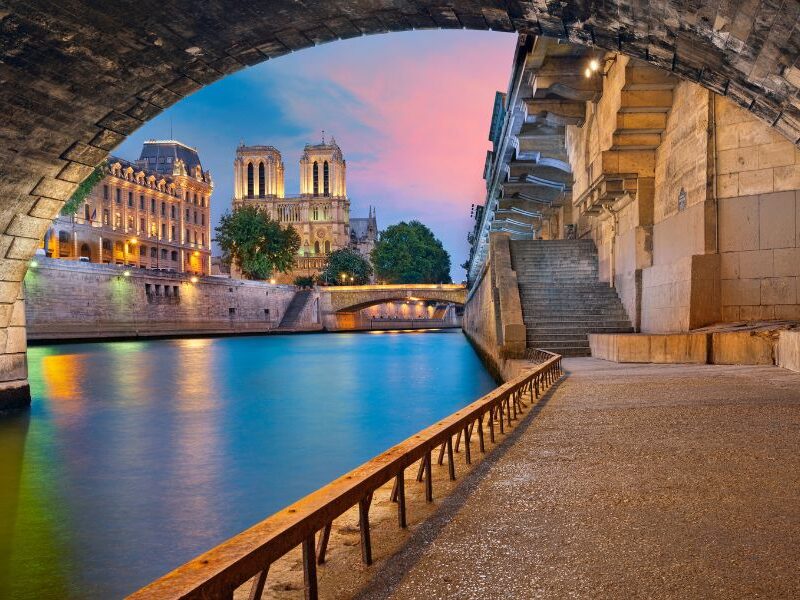 This is an image of the Seine from under a beautiful tunnel. You can see the Notre Dame in the distance and the sunset is reflecting pink on to the water.