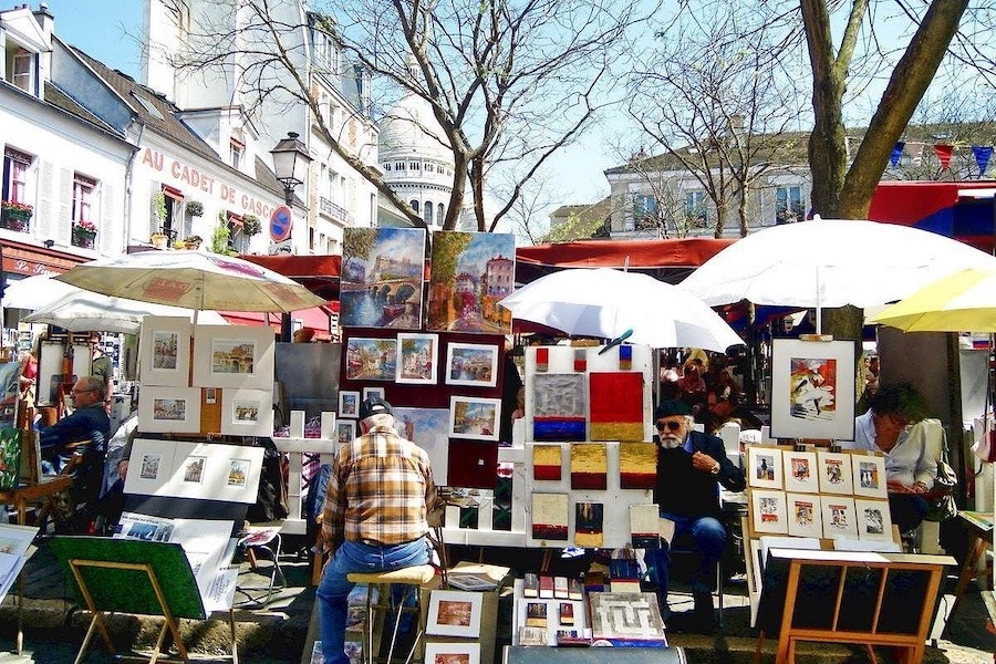 Picture shows a Montmartre artist surrounded by their paintings.