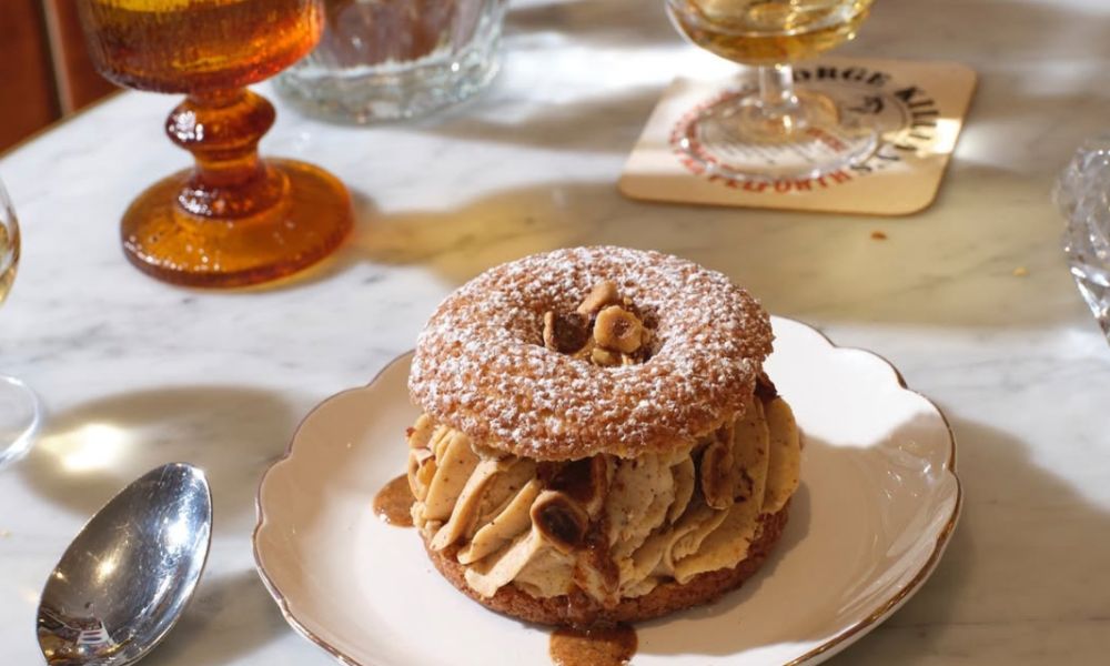 This is an image of a Paris-Brest pastry with a piped cream inside. It is on a fancy plate with a spoon.