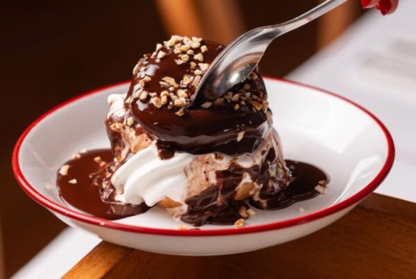 This is an image of a choux pastry with soft serve in the middle and hot chocolate sauce on top, alongside hazelnuts.