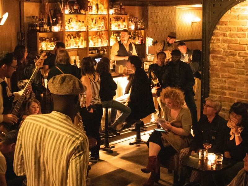This is an image of a bar with people mingling around. There is low lighting anf brick walls.