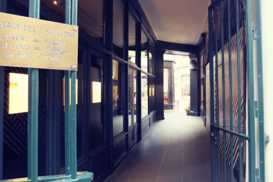 This is an image of a dark passageway in Paris with a light at the end and wooden shop fronts.