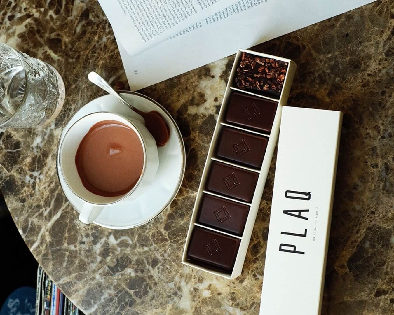 Shows a hot chocolate from Plaque, with a box of chocolates next to it.