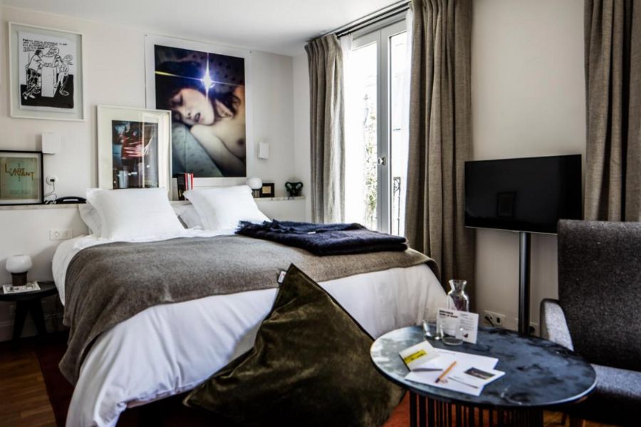 This is an image of a nice hotel room in Paris with lots of paintings and posters on the walls. Despite this, it still remains light and airy, with a TV, coffee table and more.