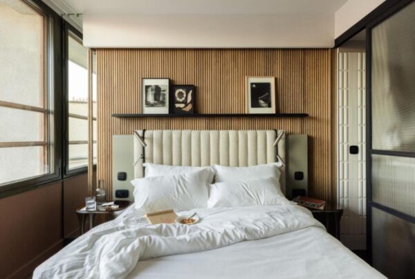 This is an image of a minimalist hotel room that looks more like a nice bedroom than accommodation. The sheets are white and there is a wooden feature wall.