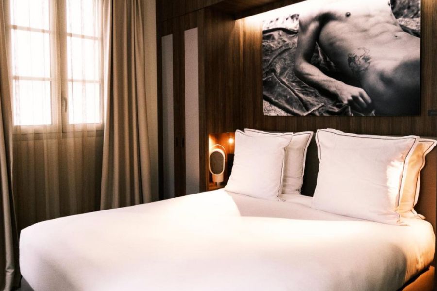 This is an image of a Jules' and Jim Hotel room which is clean and minimalist with white sheets. There is also a big piece of art above the bed featuring someone's torso.