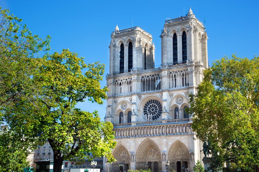 This is an image of the front of the Notre-Dame in front of a blue sky and greenery.
