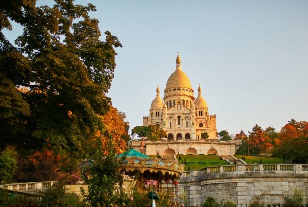 This is an image of the Sacre-Coeur on a hill during sunset time with greenery surrounding.