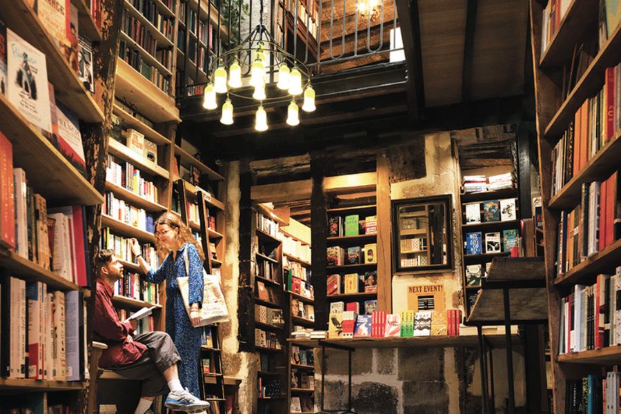 This is an image of a lady browsing a bookstore full from floor to ceiling with stacked books.