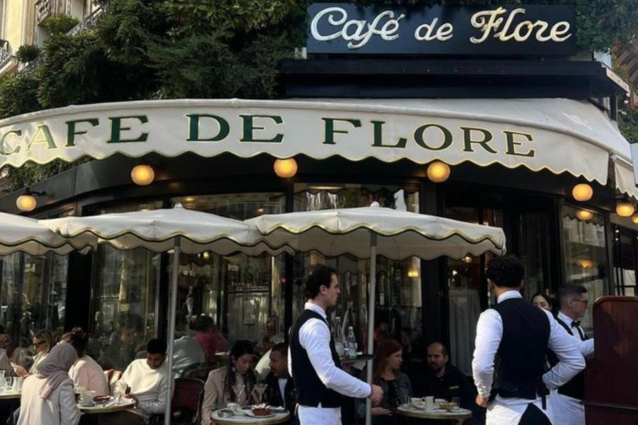 Best literary spots in Paris: This is an image of the front of Cafe de Flore, an iconic cafe in Paris, with servers out the front and lots of people sitting on the tables outside.