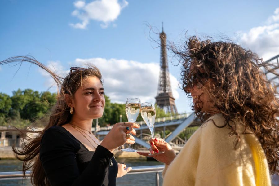 Two friends toasting with champagne flutes on a Seine river cruise, Eiffel Tower in the background