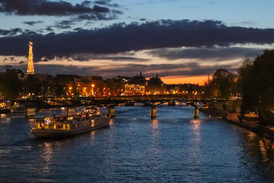 Sunset over the Seine with a dinner cruise boat passing beneath Parisian bridges, Eiffel Tower lit up in the distance