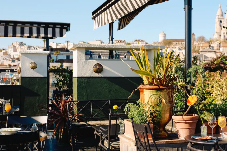 A sunny rooftop terrace with potted plants and a view of Sacré-Cœur in the distance