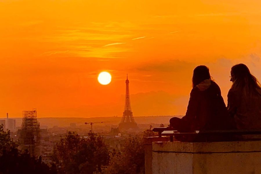 Two friends watching the sunset over Paris, with the Eiffel Tower silhouetted in the distance