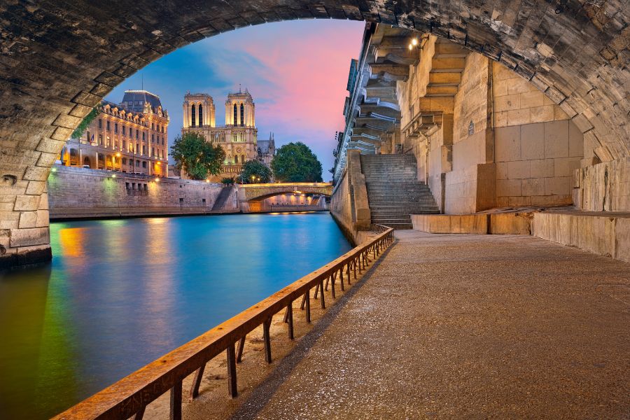 View of Notre-Dame Cathedral and the Seine from beneath a stone bridge at dusk