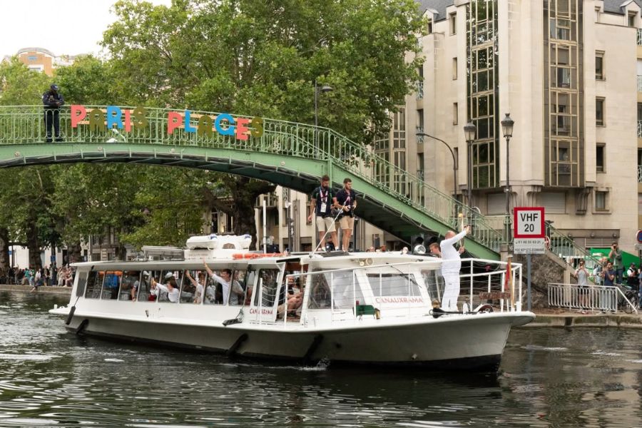 A Canauxrama canal boat cruising along Canal Saint-Martin, passing under a footbridge in Paris