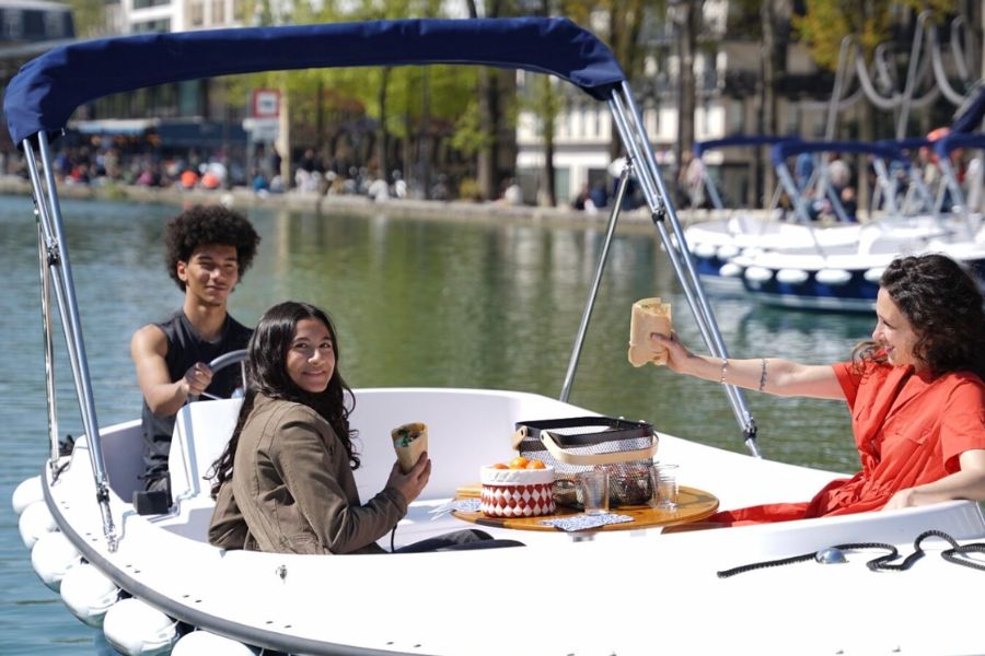 Friends sharing crepes aboard an electric picnic boat on the Canal de l'Ourcq
