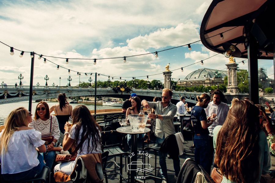 People enjoying drinks on a riverside rooftop terrace overlooking the Seine and Pont Alexandre III