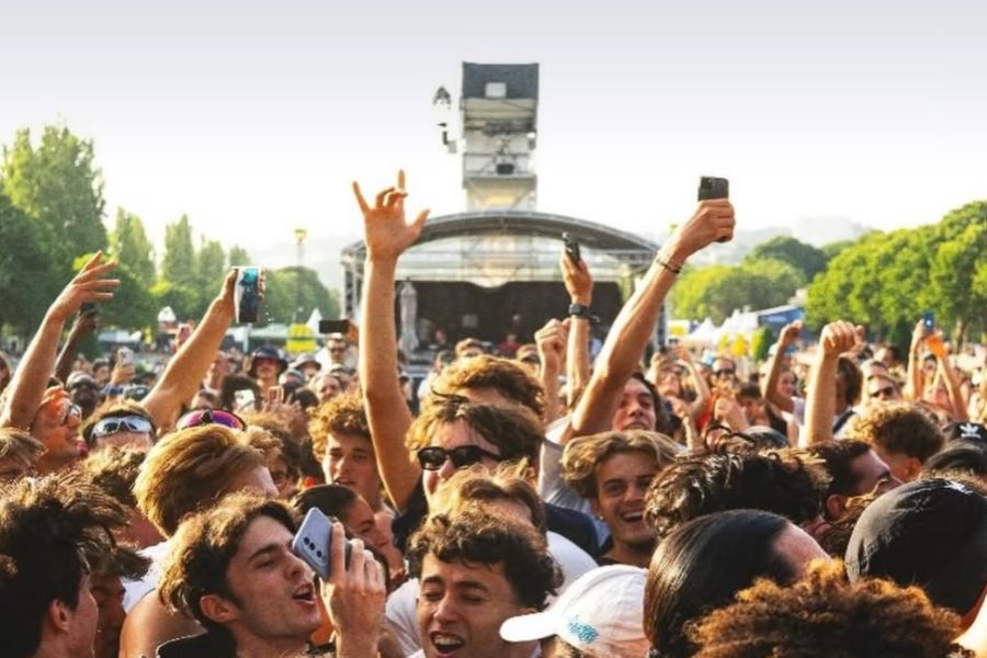 A festival crowd with arms raised and phones out in front of an outdoor stage