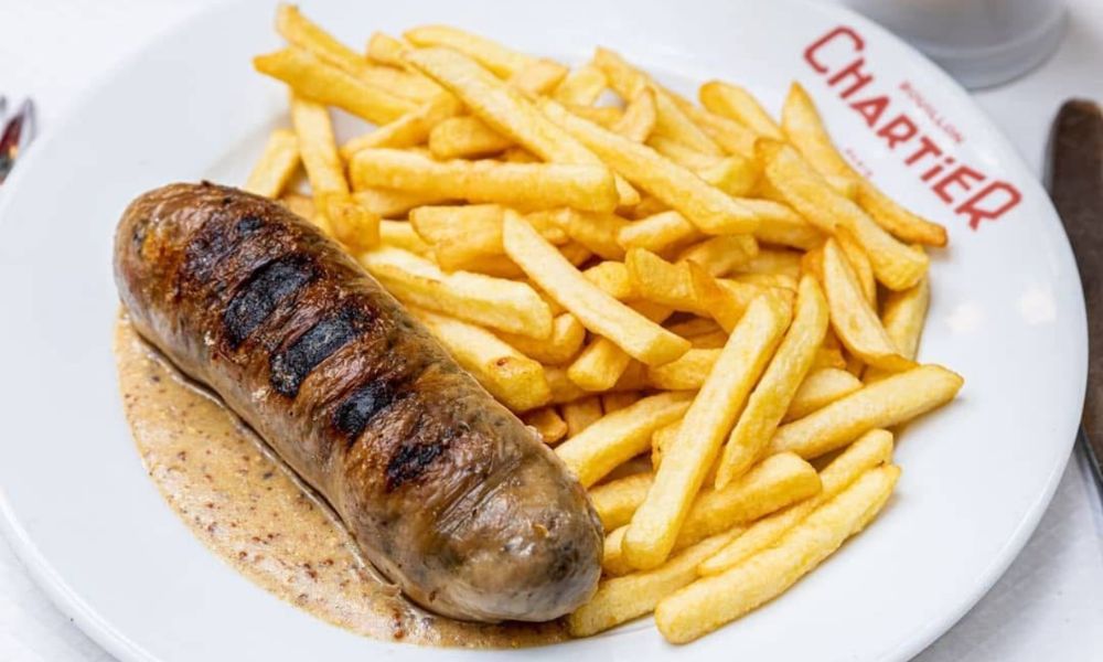 This is an image of a sausage on a plate with fries and sauce.