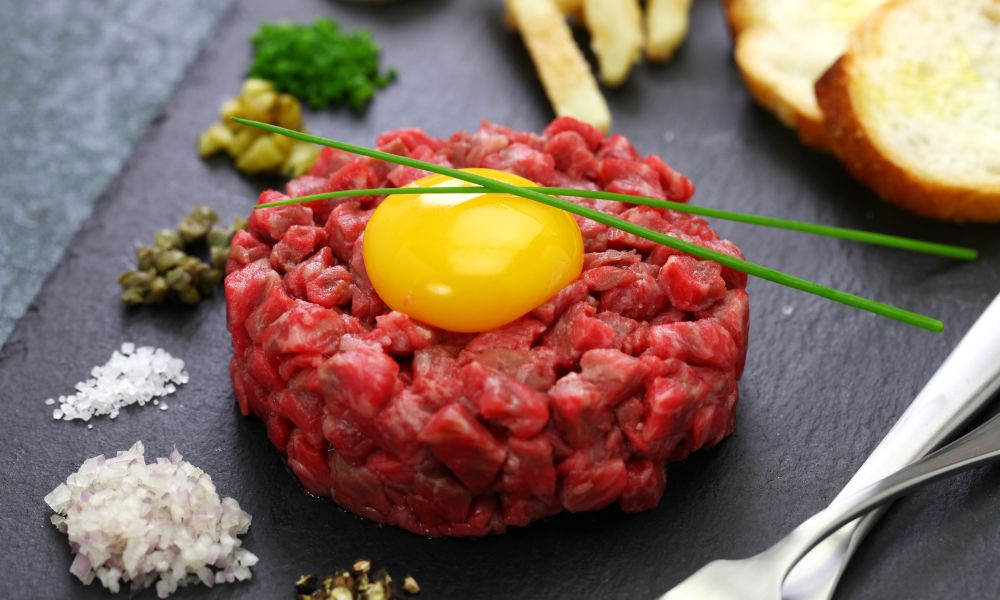 This is an image of beef tartare with an egg yolk on top and a bunch of spices.