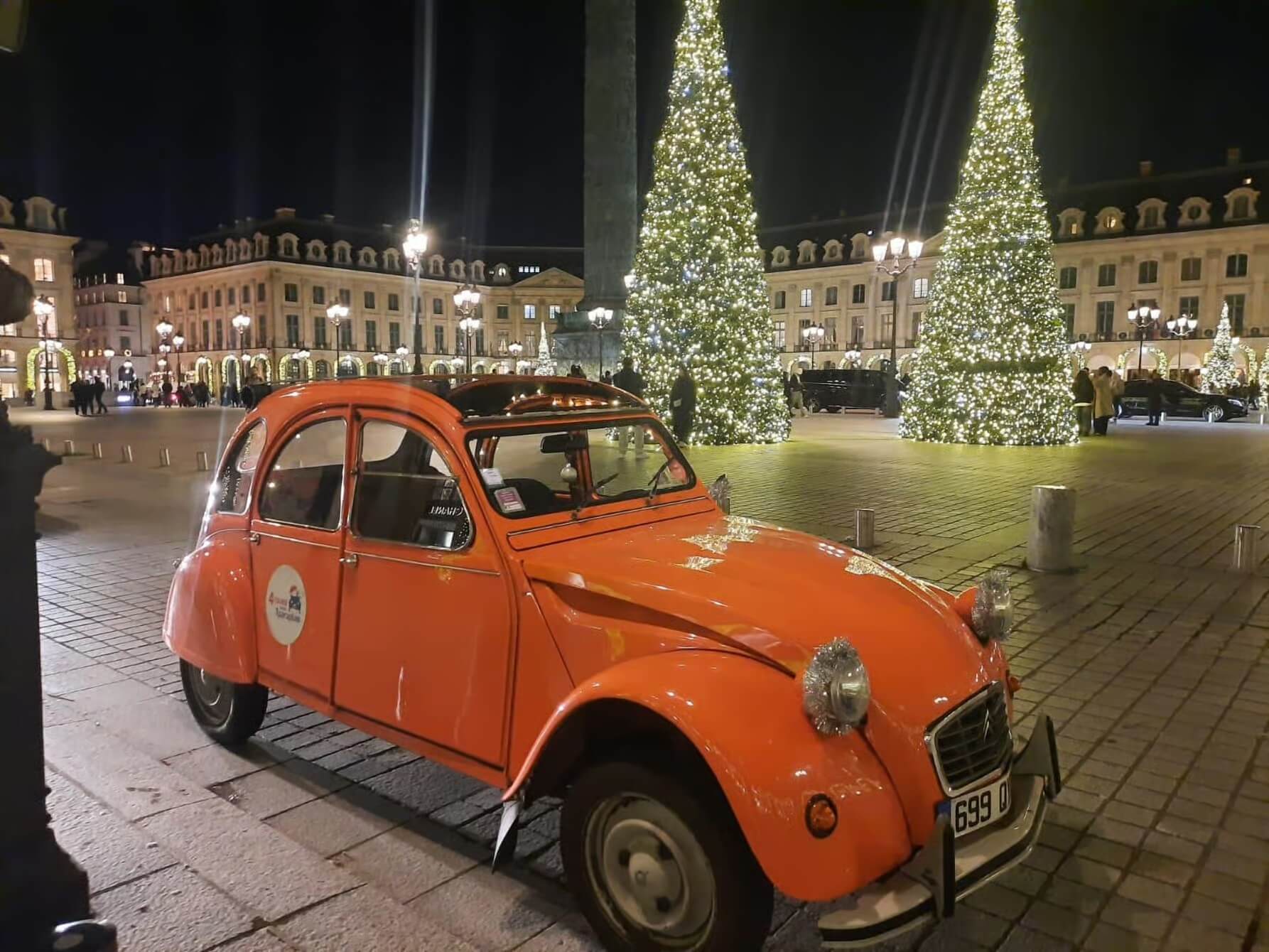 This picture shows an orange citroen car, with two christmas trees in the background.