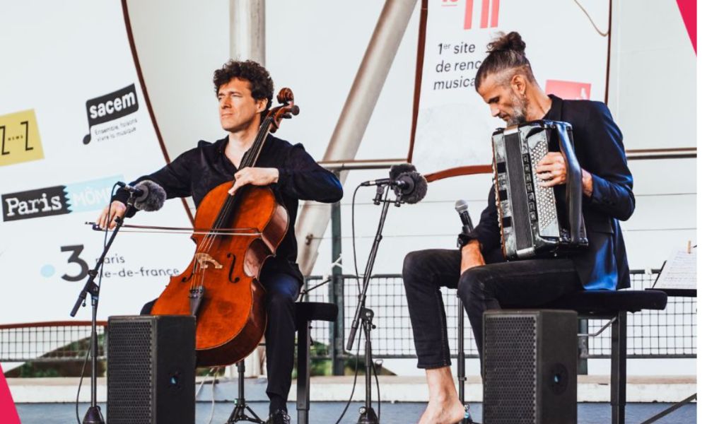 This is an image of two musicians on a stage. One is playing the violin and the other a harmonica.