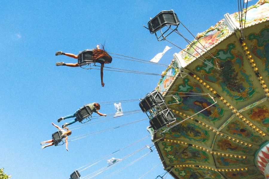This is an image of kids swinging around on a big ride in chairs. There is a blue sky in the background.
