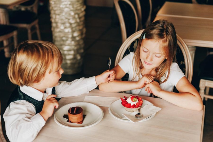 This is an image of two kids sitting at a table, each with a dessert in front of them. They are waiting patiently to eat it.