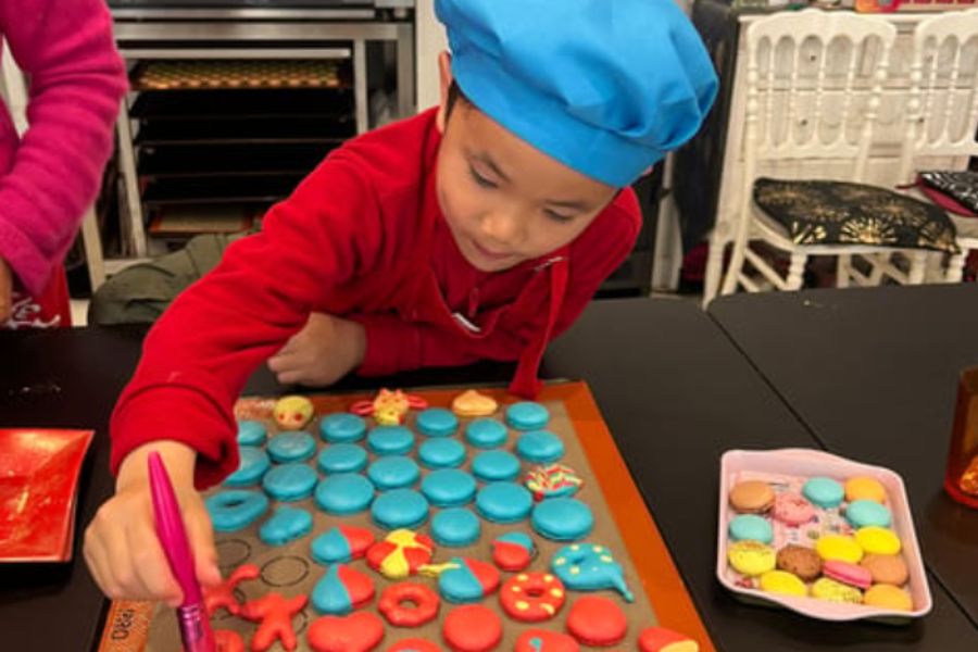 This is an image of a little boy in a chef's hat decorating very colourful macarons.
