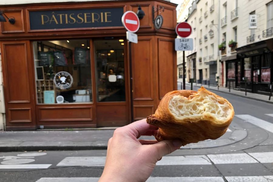 This is a picture of a person holding a croissant in front of a patisserie.