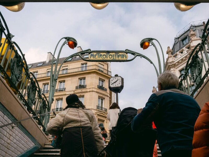 This is an image of commuters exiting the Paris metro. There is a big avantgarde 'Metropolitan' sign on the way out.