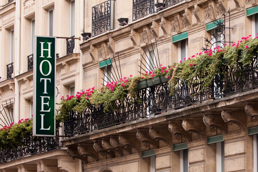 This is an image of a hotel front with little balconies full of flowers and a big 'hotel' sign.