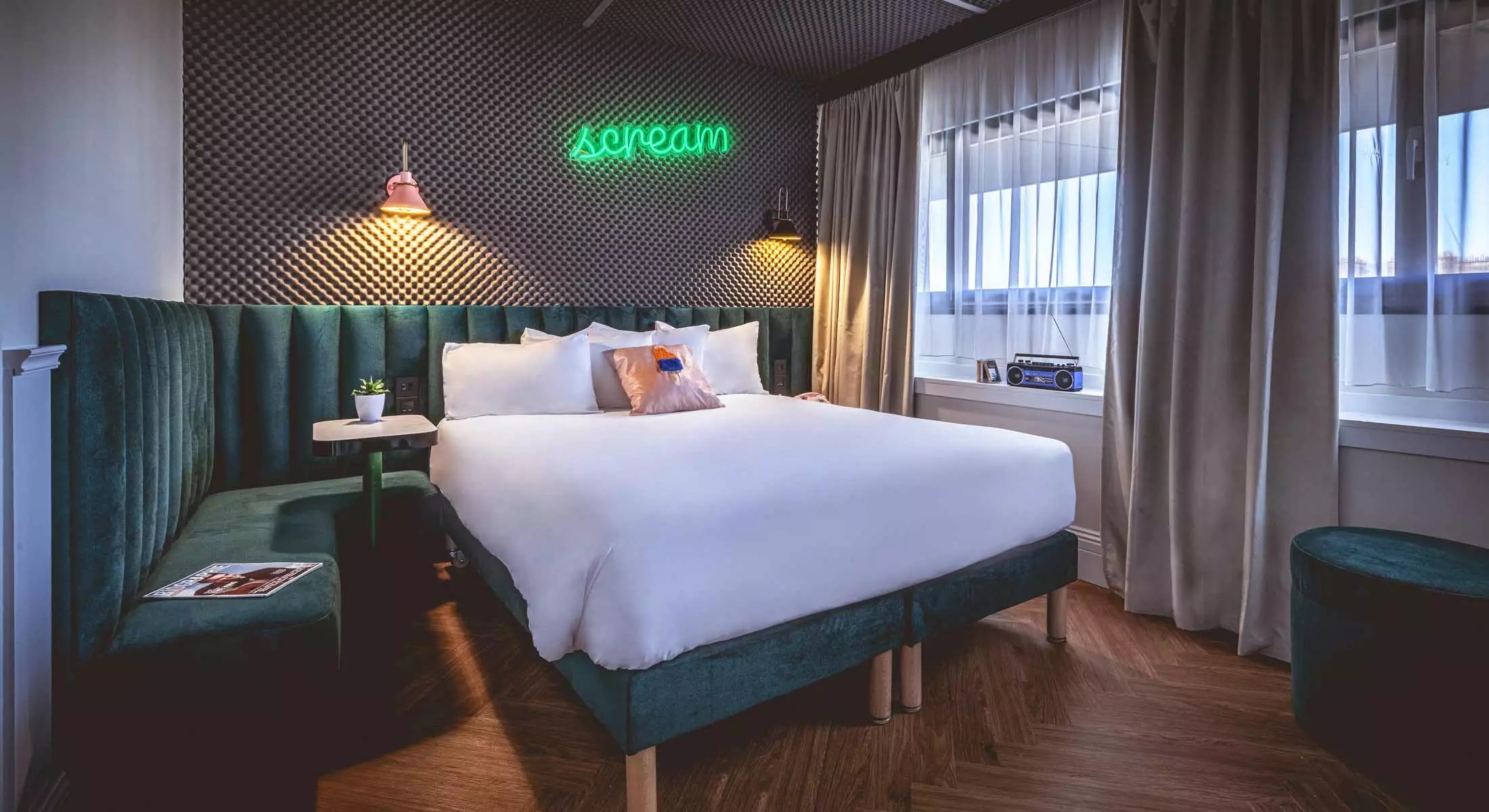 This is an image of a hotel bedroom with a big double bed with white sheets and windows with taupe curtains and wooden floors. This is a great Budget Friendly Hotels in Paris.