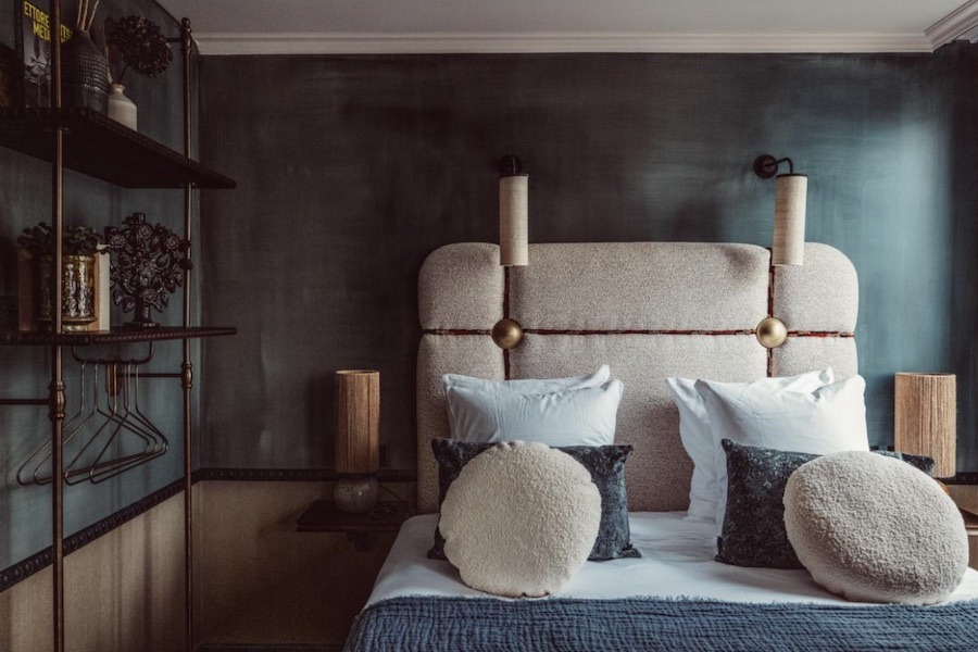 This is an image of a rustic hotel room with a double bed and cushions in a dusty blue colour.