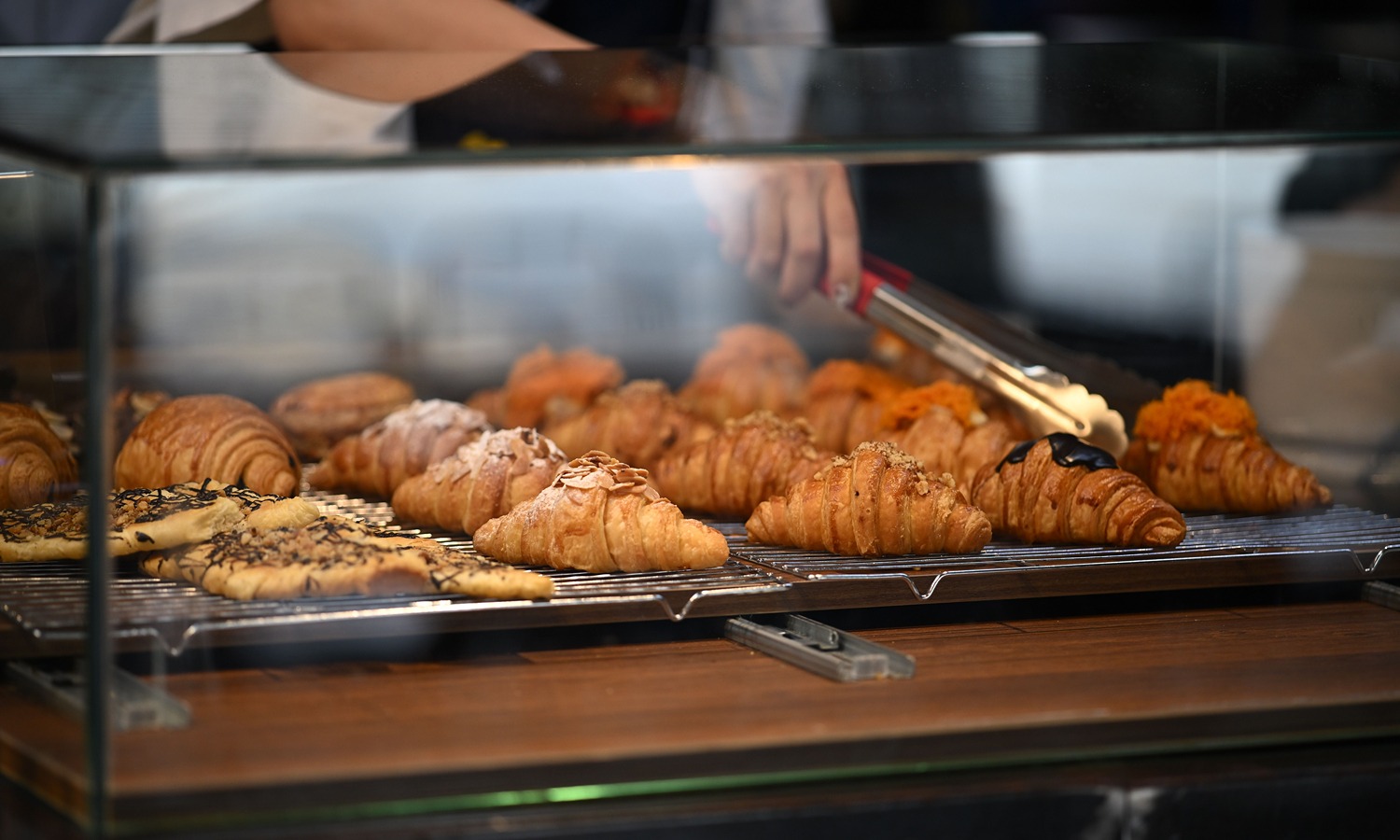 Bakery display window in Paris showing croissants and chocolate chip rolls, seen through reflective glass.